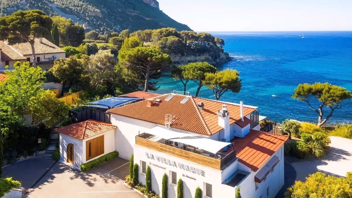Maison blanche avec toit rouge près d'une côte rocheuse et d'une mer bleue sous un ciel clair