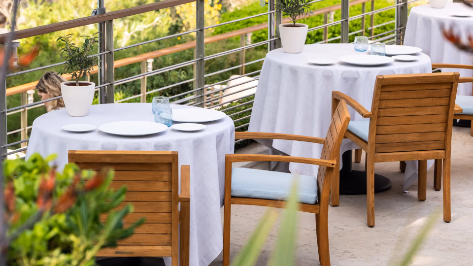 Terrasse de restaurant avec tables rondes couvertes de nappes blanches, chaises en bois et vue sur un paysage verdoyant